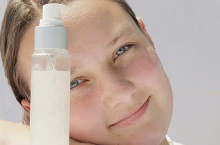 A teen smiling behind skincare bottles