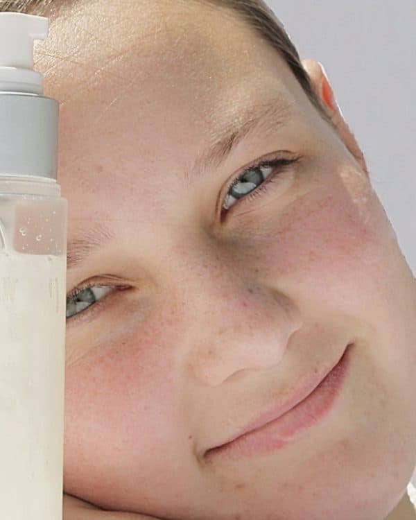 A teen smiling behind skincare bottles